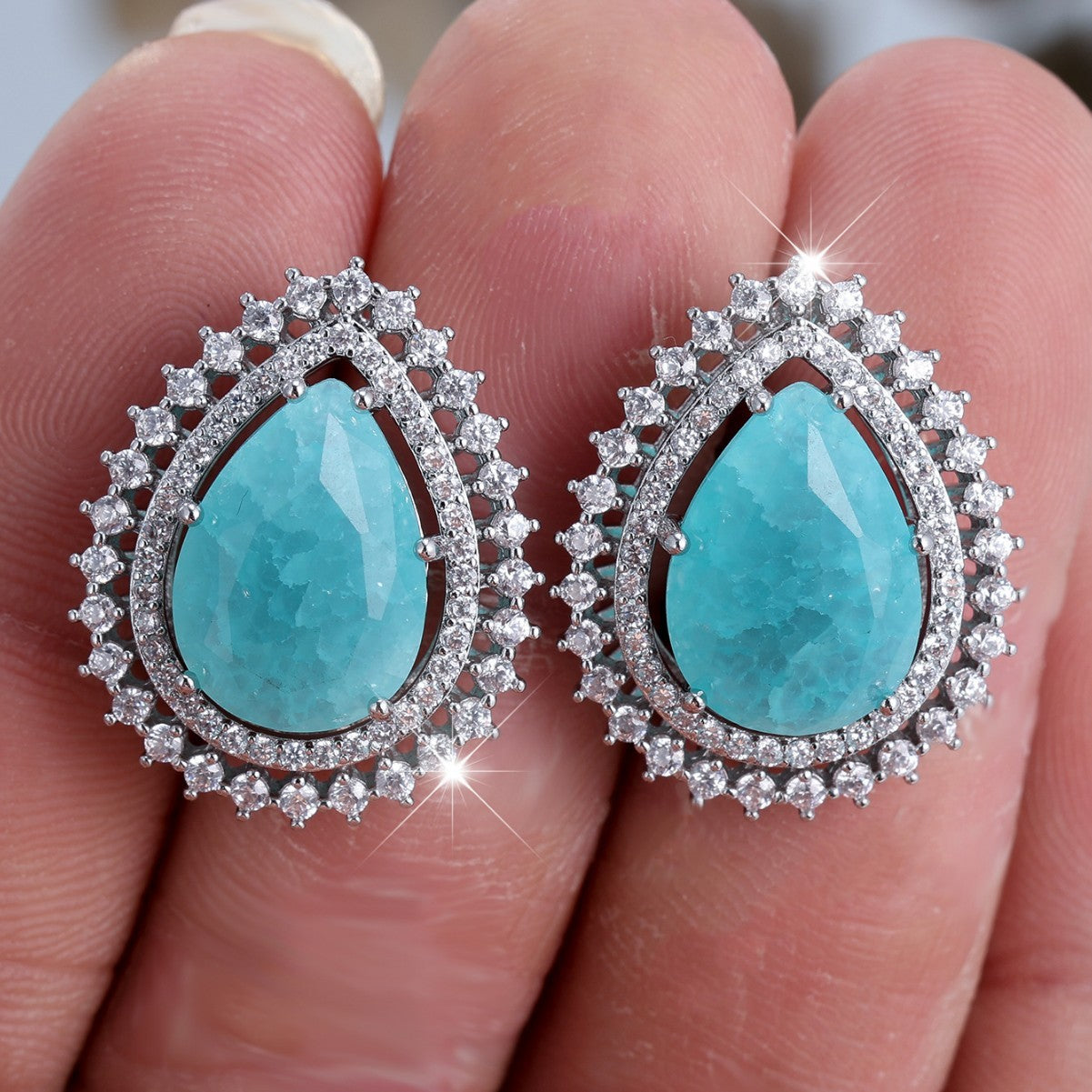 Turquoise teardrop earrings with silver accents held between fingers.
