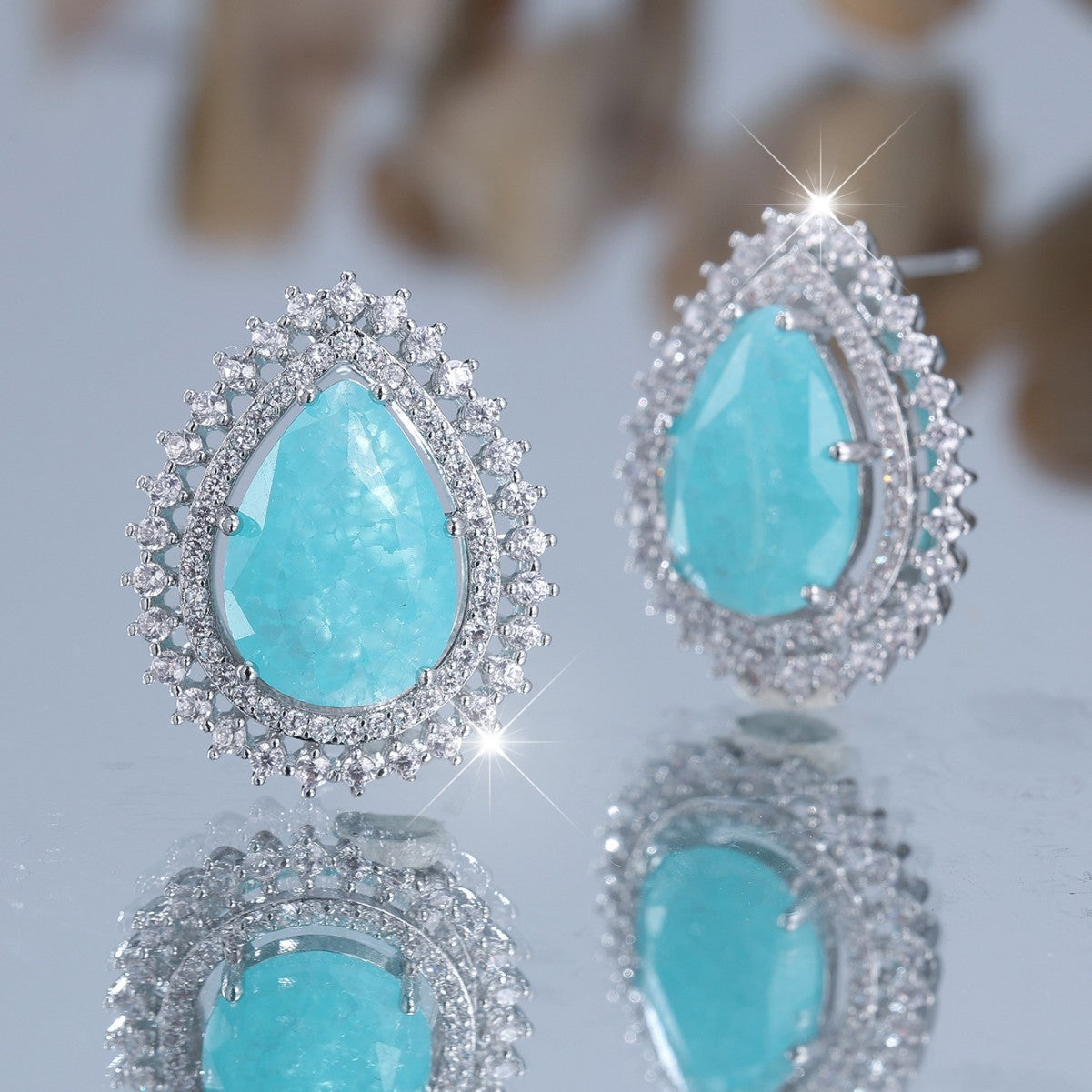 Turquoise teardrop earrings with silver frames on a reflective surface