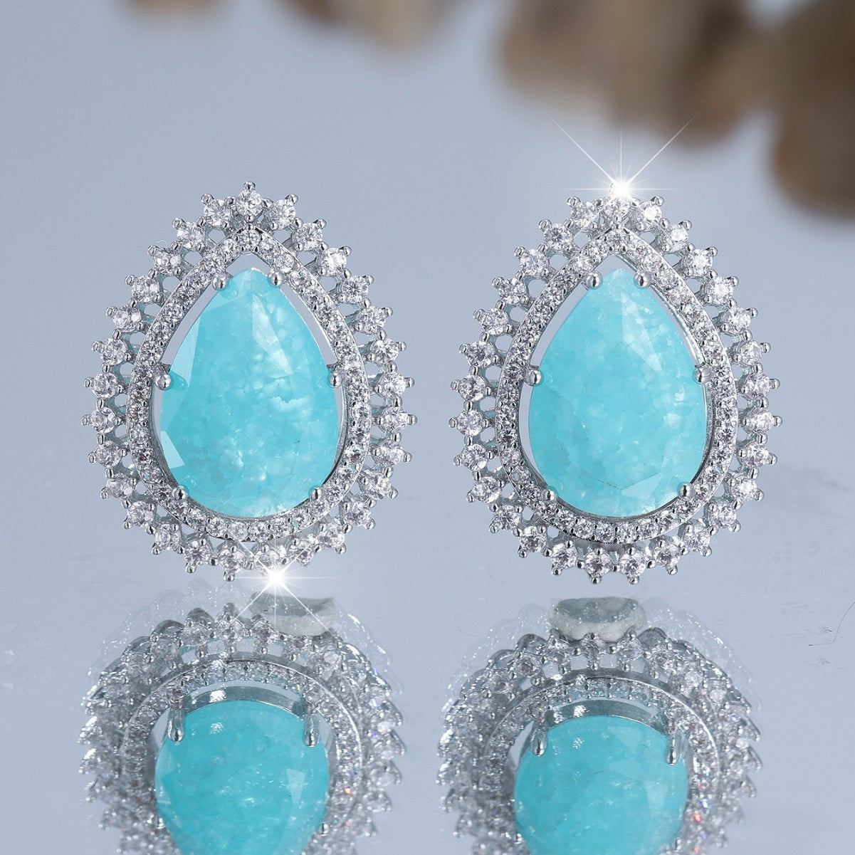 Turquoise teardrop earrings with silver accents on a light gray background