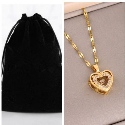 Gold heart-shaped necklace with chain on a gray surface next to a black velvet pouch. women’s necklace with rhinestones