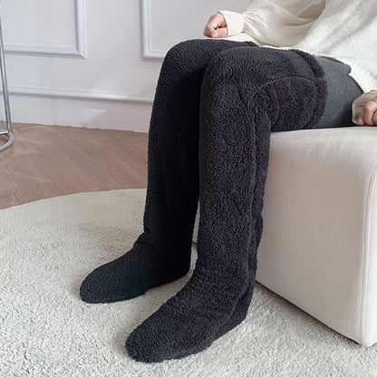 Person wearing black fuzzy socks sitting on a white couch.