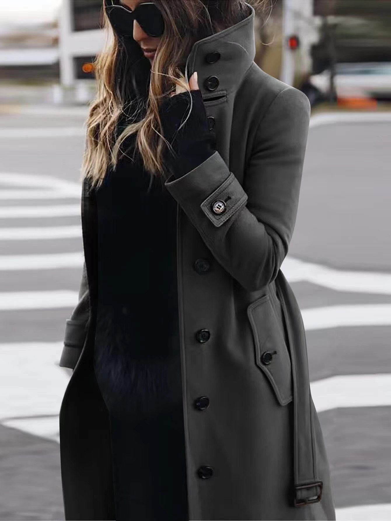 Woman wearing a long gray coat and black gloves on a city street.