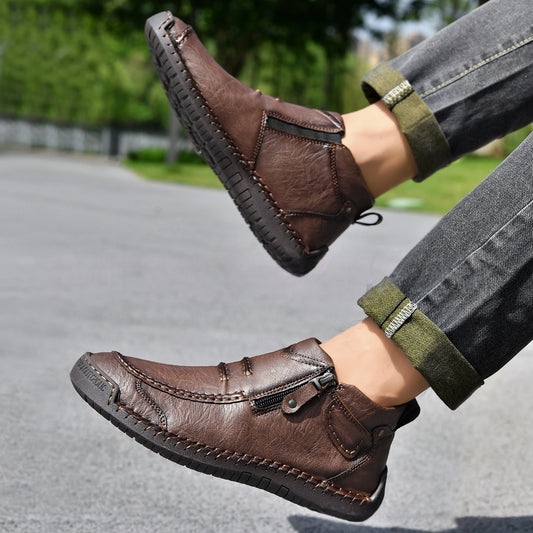 Brown leather shoes worn with gray jeans and green cuffs, on a blurred outdoor background.