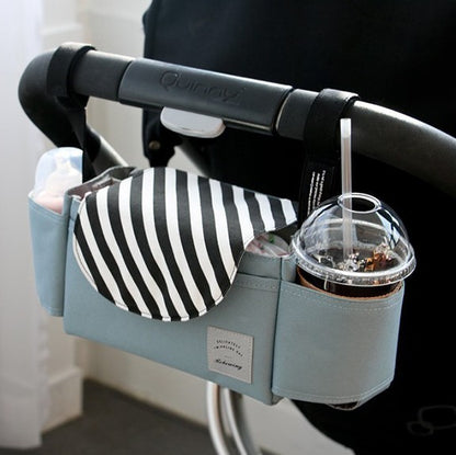 Stroller organizer with cup holder and striped pouch attached to a stroller handle.